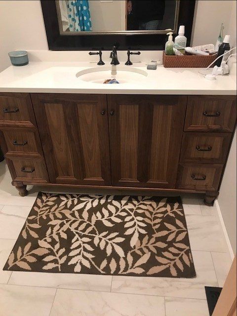 Bathroom vanity with white sink, dark wood cabinets, mirror, and leaf-patterned rug