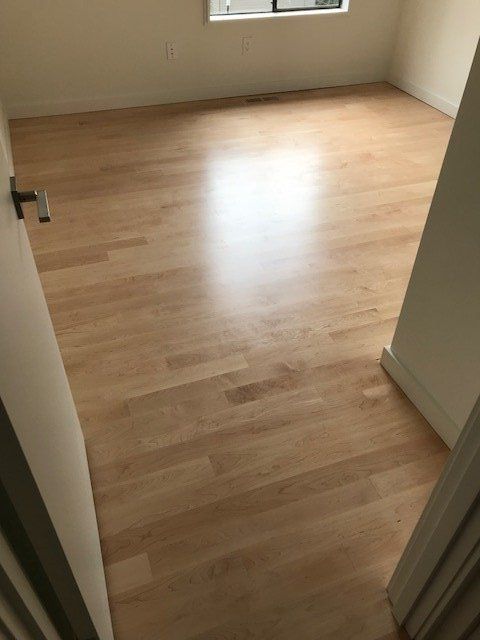 Empty light-wood-floored room with beige walls and a window.