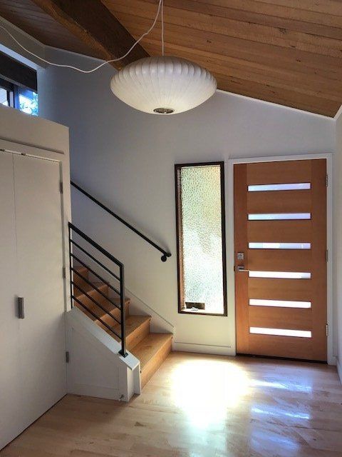 Modern entryway with wooden door, staircase, frosted window, and sunlight on hardwood floor