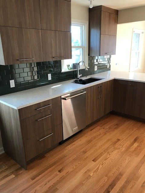 Modern kitchen with wood cabinets, stainless-steel dishwasher, dark tile backsplash, and hardwood floor