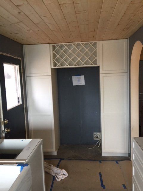Empty room with dark front door, white built-in cabinets, and a wooden ceiling; a kitchen counter is in the foreground