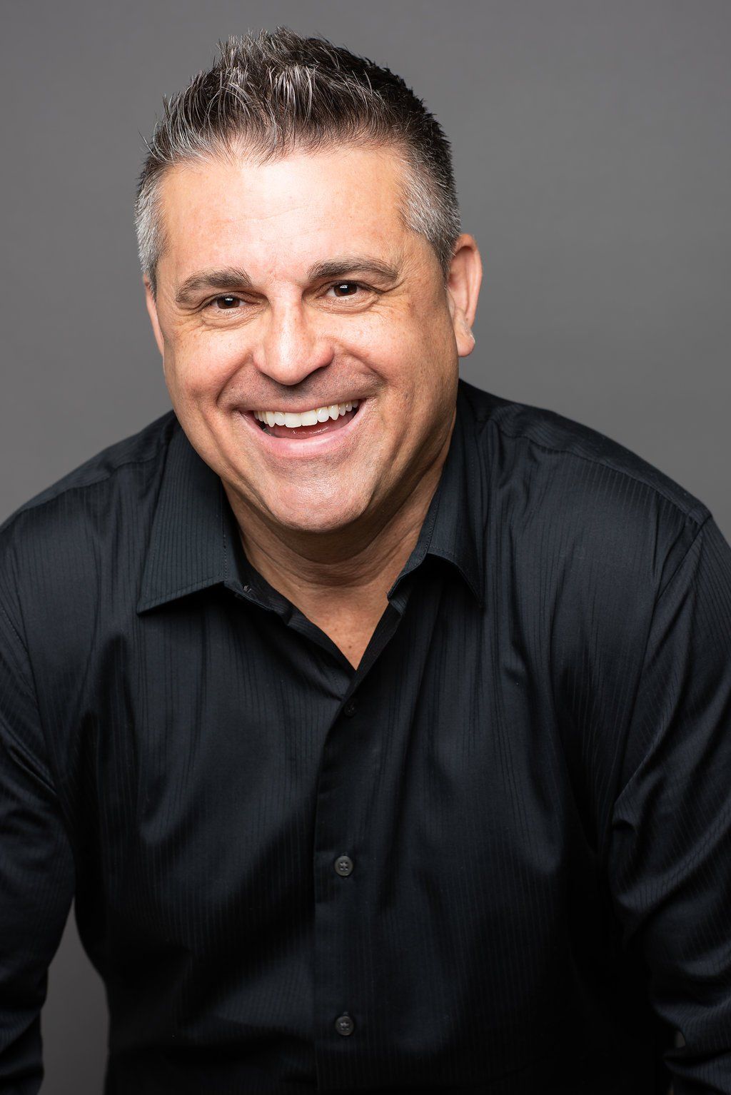 Smiling man in a black shirt posing against a gray studio background