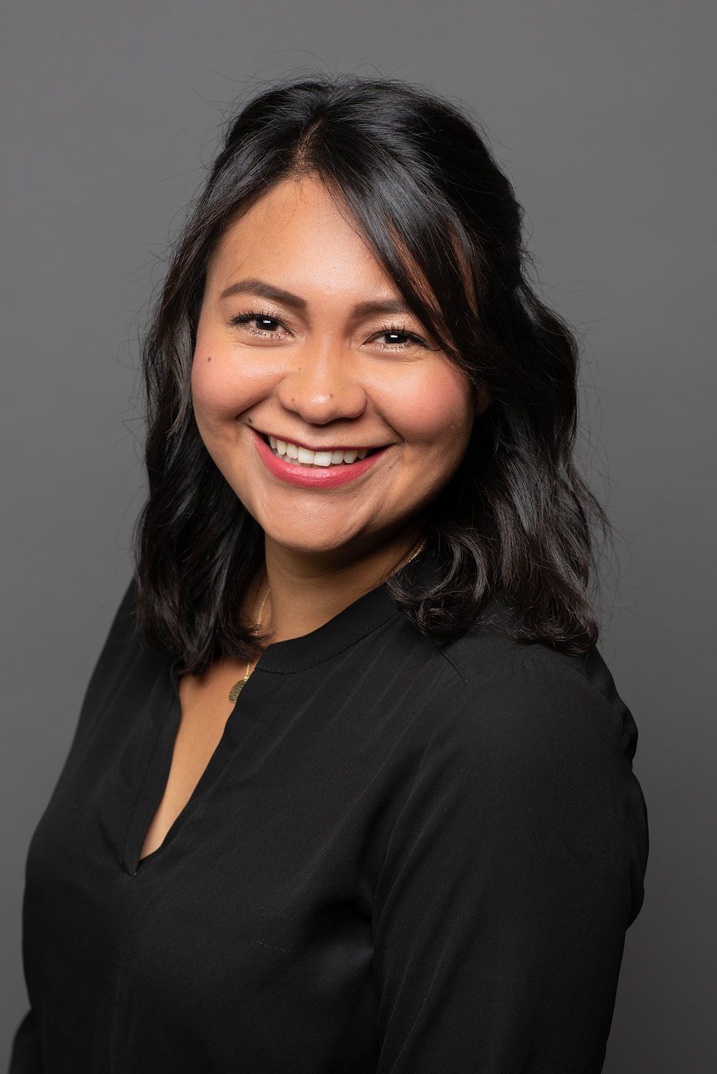 Smiling woman in a black top against a gray studio background