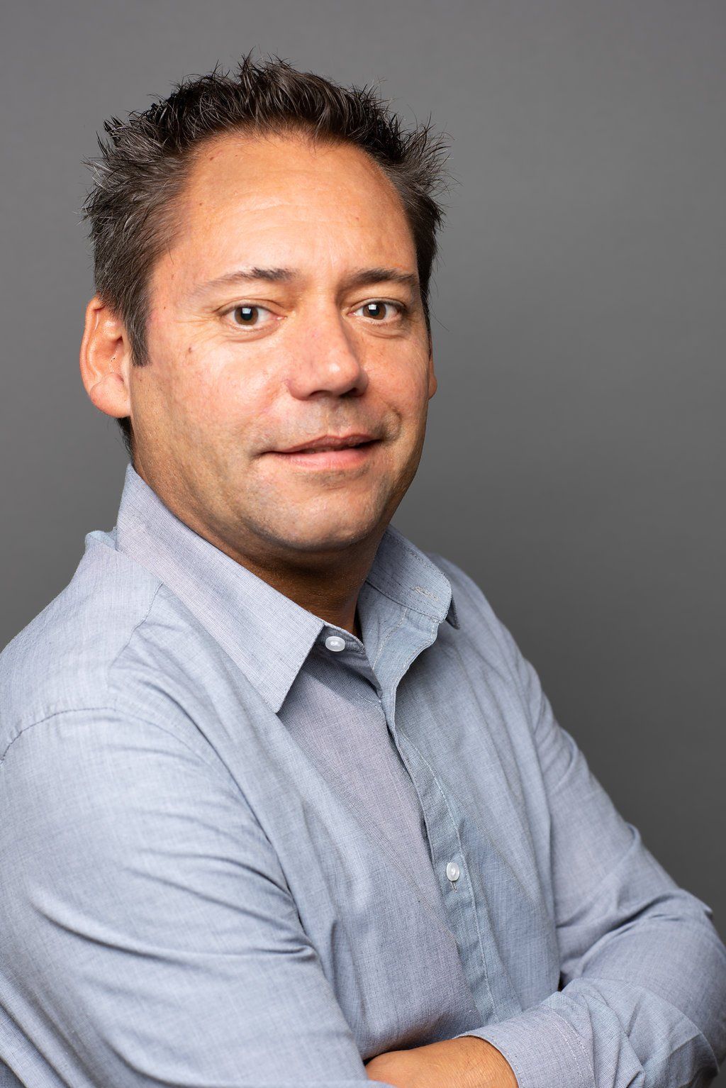 Portrait of a person in a light blue shirt with arms crossed against a gray background