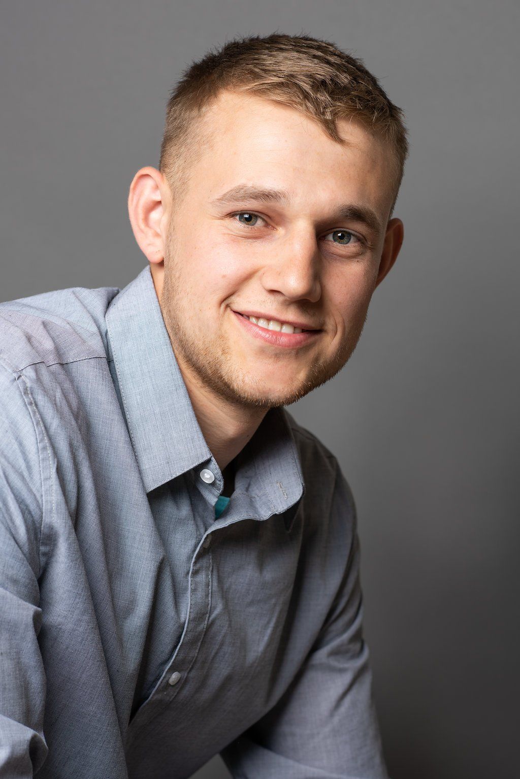 Smiling person in a light blue shirt against a gray studio backdrop