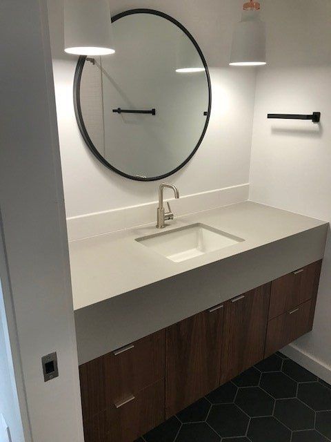 Modern bathroom vanity with round mirror, white countertop, and dark wood cabinets, black hex tile floor
