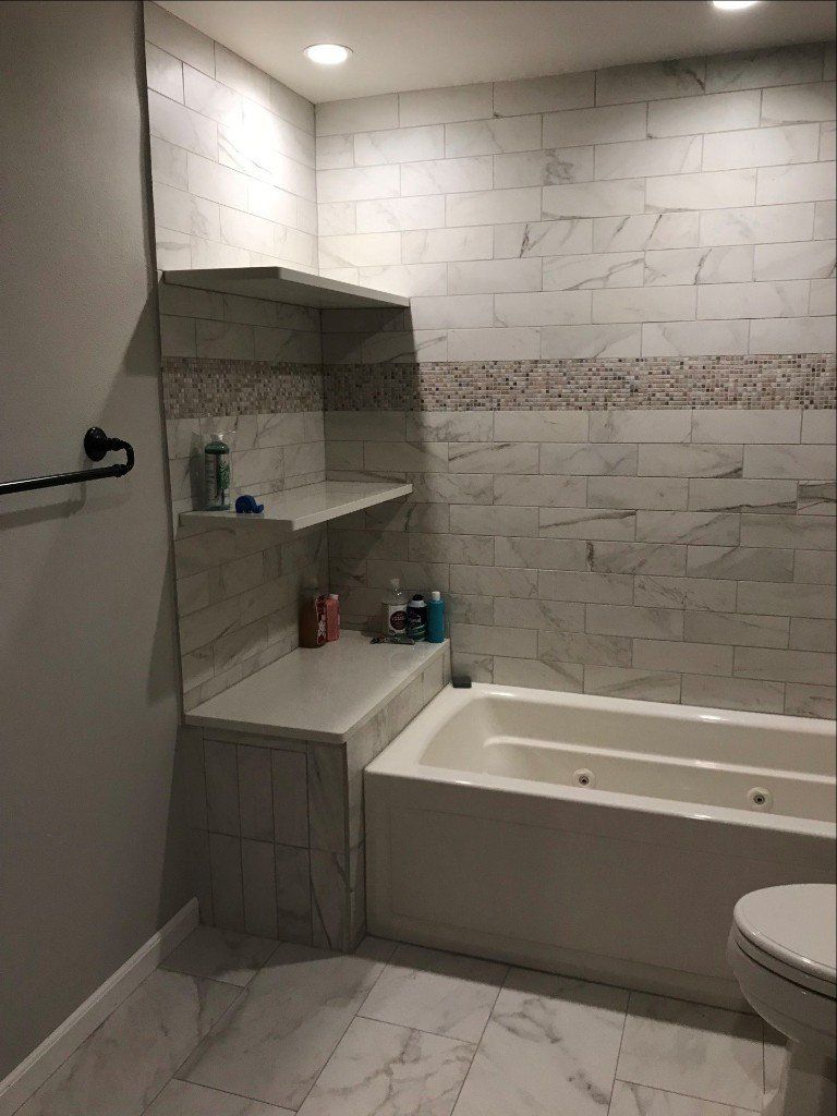 Small white tiled bathroom with a bathtub-shower, built-in shelves, and a partial toilet visible.