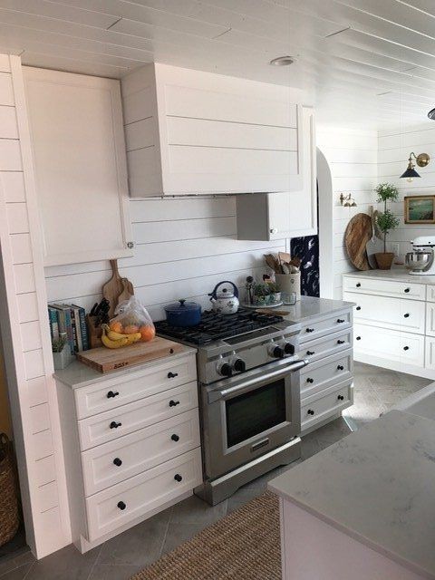 Bright white kitchen with a stainless stove, white cabinets, and countertop clutter