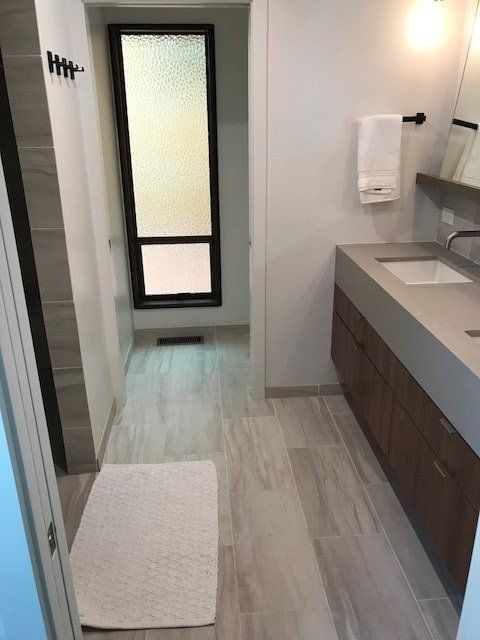 Narrow bathroom with sink vanity, frosted door, and white bath mat on pale wood floor