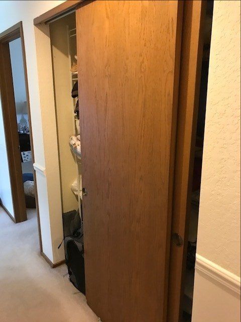 Partially open wooden closet door in a hallway, with a person barely visible inside