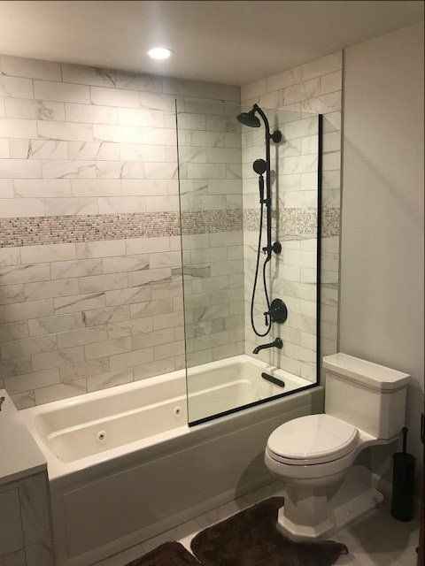 Modern bathroom with tiled walls, glass shower, white tub, toilet, and recessed lighting