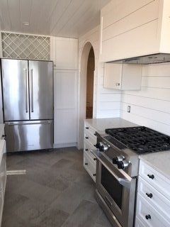 Bright white kitchen with stainless steel fridge, gas stove, and tiled floor, viewed from the doorway