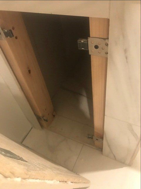 Partially open wooden cabinet door revealing a dark interior in a tiled room