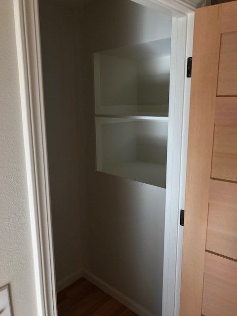 Open closet or pantry with white shelves and wood floor, viewed through a partially open door