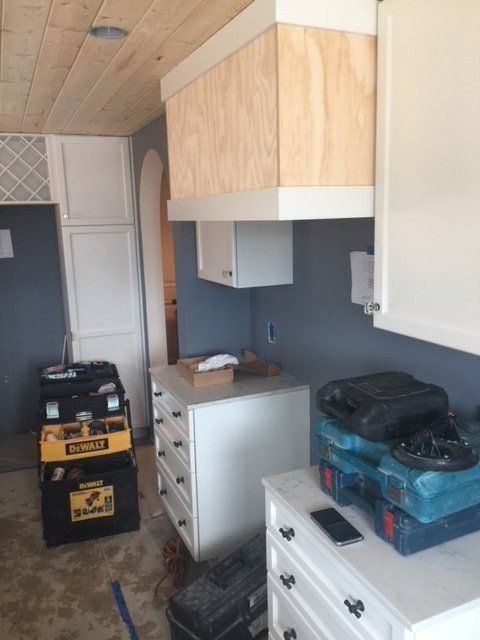 Narrow storage hallway with cabinets, drawers, boxes, and a yellow machine on a floor under renovation