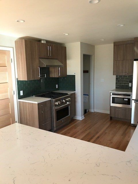 Modern kitchen with wood cabinets, dark tile backsplash, stainless appliances, and light wood floors