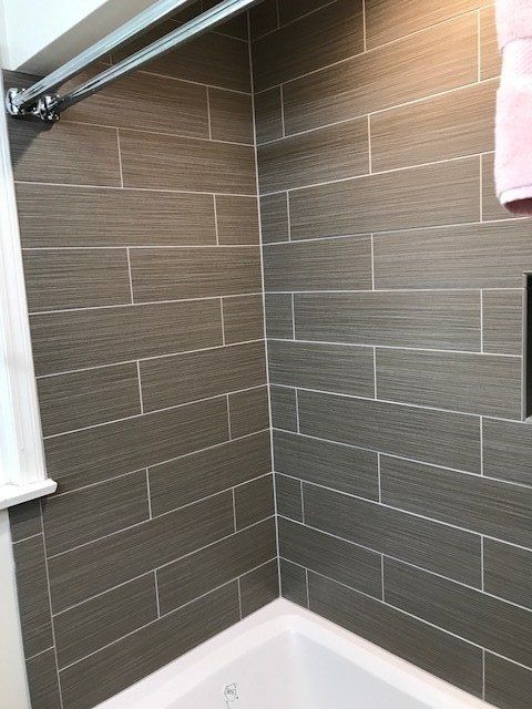 Tiled shower corner with gray walls, white tub edge, and a shower rod above