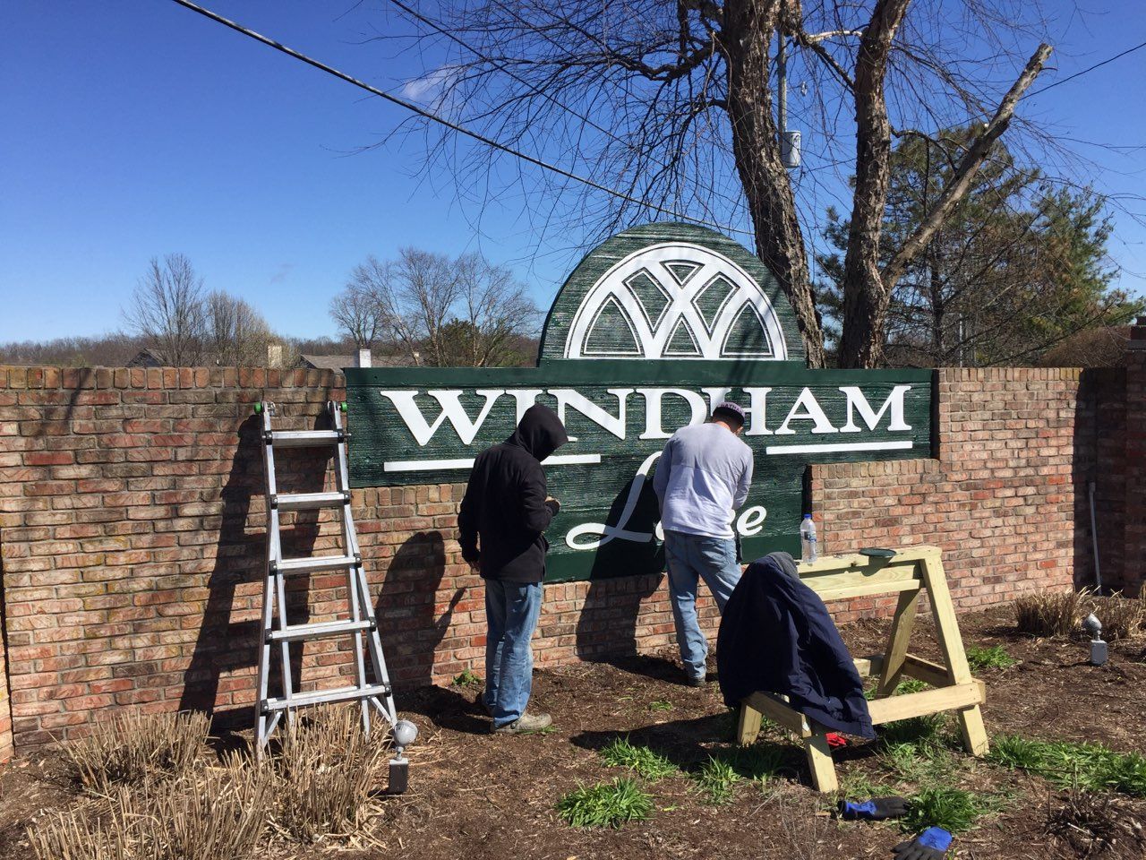 Two men are installing a windham sign on a brick wall.