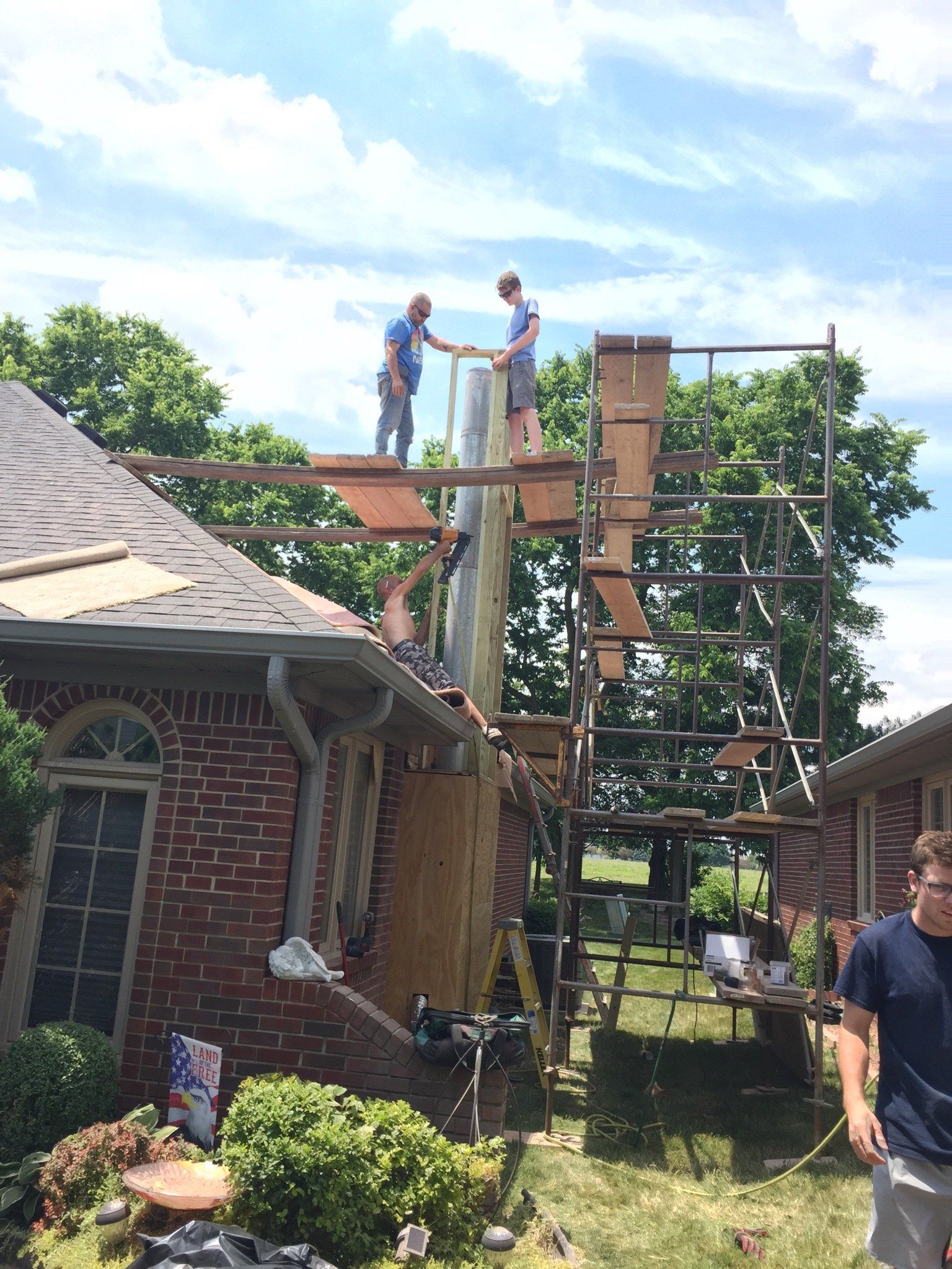A group of men are working on a chimney on top of a brick house.