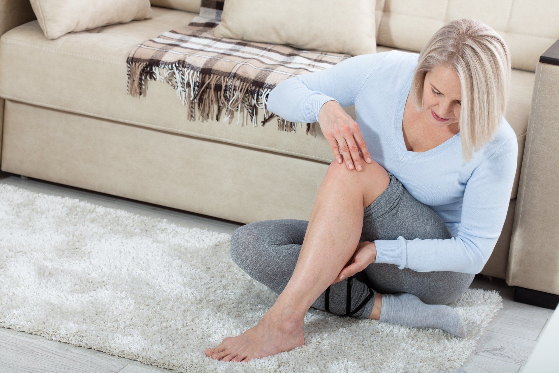 A woman is sitting on the floor holding her knee in pain.