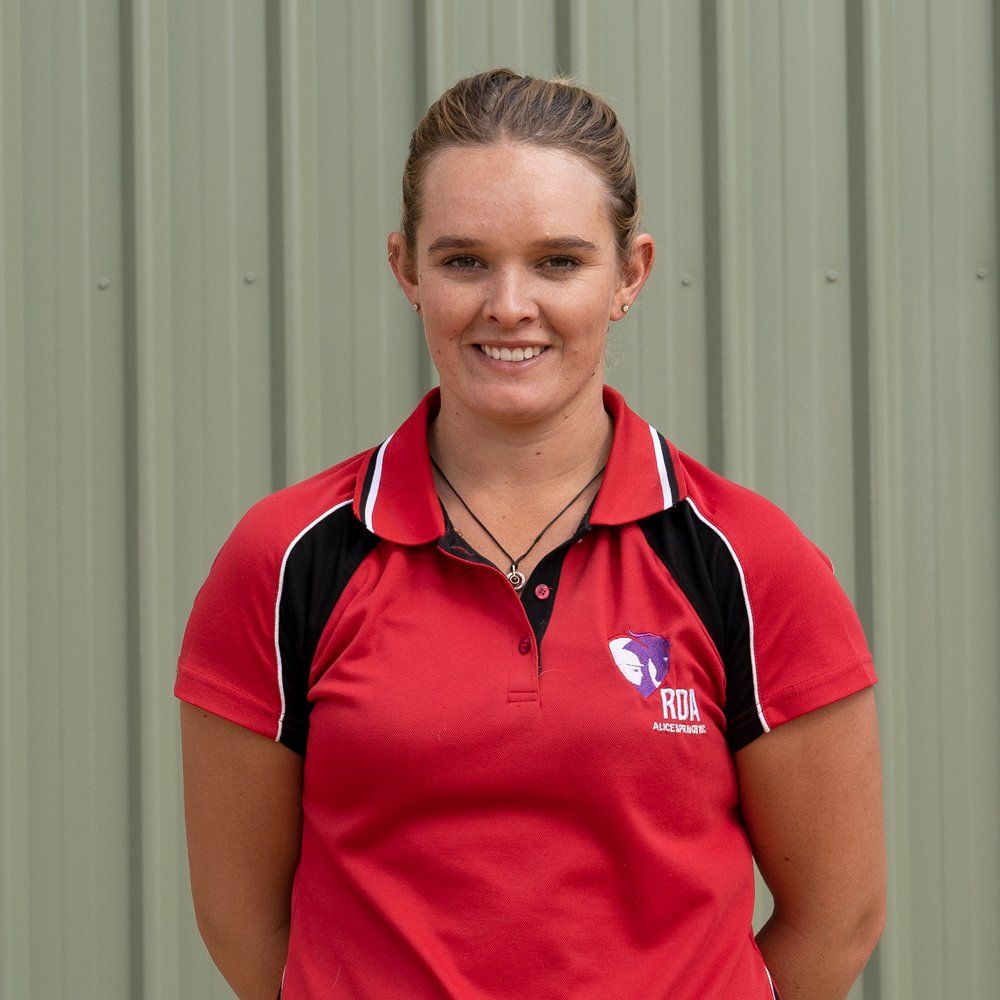 Woman in red polo shirt smiles, standing in front of a green wall. She has blonde hair pulled back.