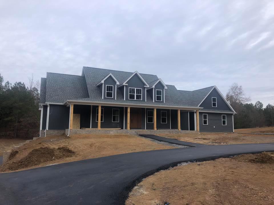 A large house with a large porch is sitting on top of a dirt field.