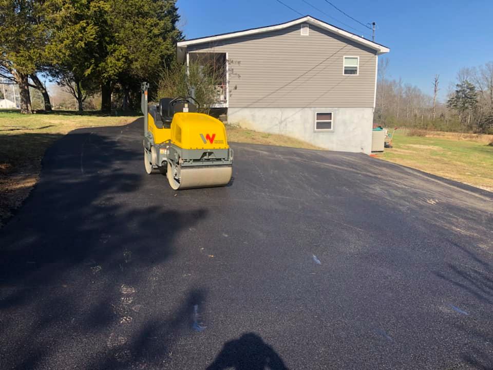 A yellow roller is driving down a road in front of a house.