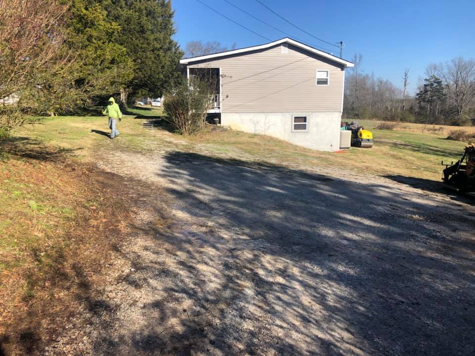A man is walking down a dirt road in front of a house.