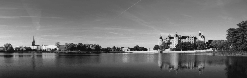 Ein Schwarzweißfoto eines Sees mit einem Schloss im Hintergrund.