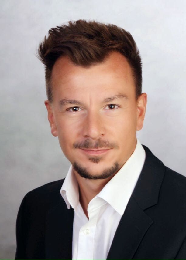 Un uomo con la barba indossa un abito e una camicia bianca.