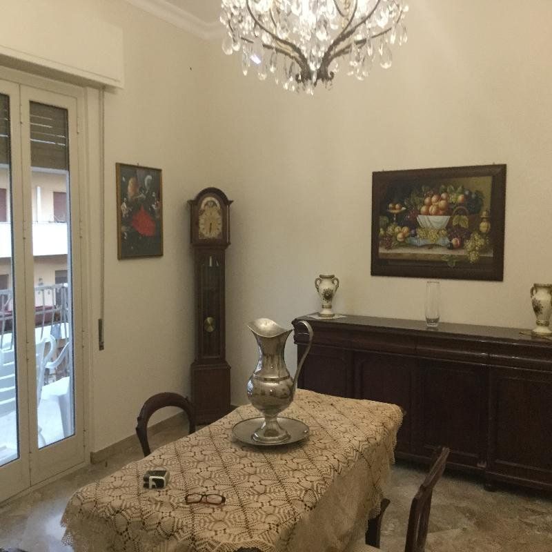 Elegante sala da pranzo con lampadario, orologio a pendolo, quadri incorniciati e tavolo apparecchiato con vaso d'argento.