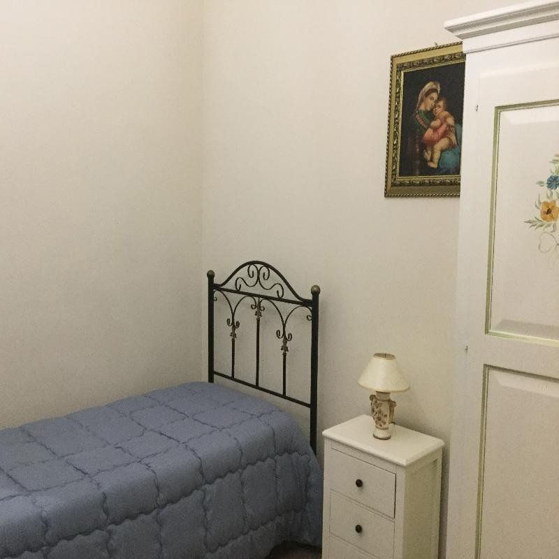 Piccola camera da letto con copriletto blu, testiera in metallo nero, comodino bianco e quadri appesi alla parete.