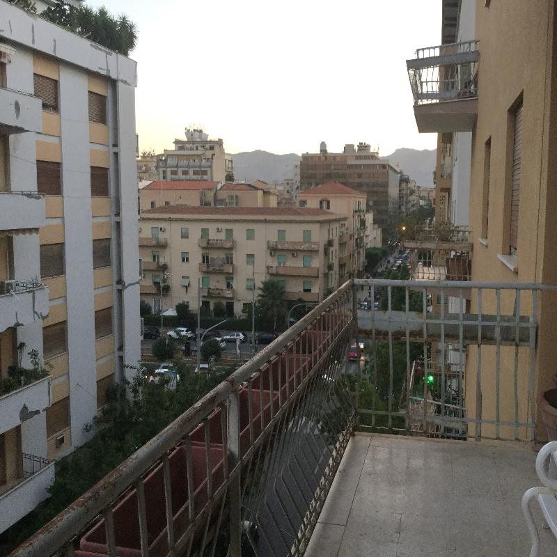 Vista dal balcone su una strada cittadina con palazzi e colline in lontananza al crepuscolo