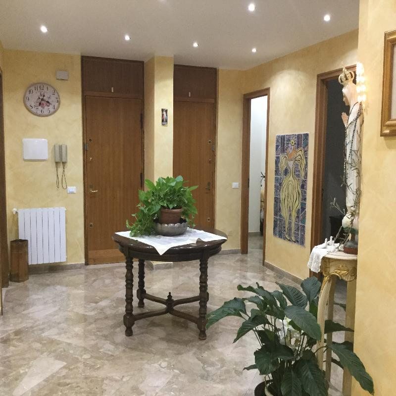 Luminoso corridoio con un tavolo in legno e piante in vaso, quadri alle pareti, un orologio e faretti a incasso sul soffitto.