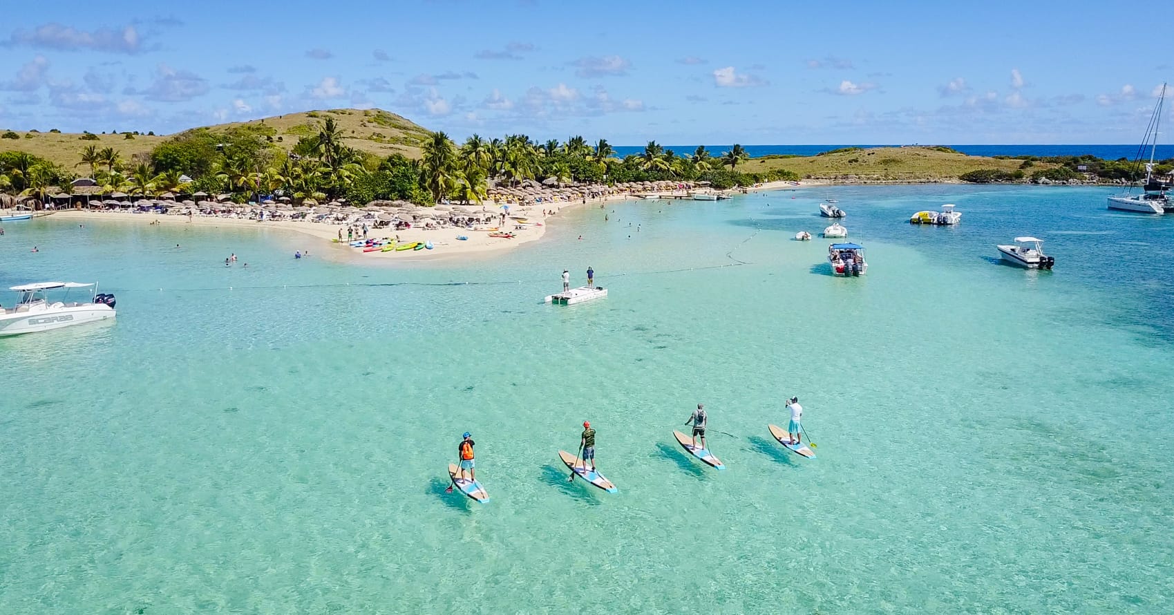 Four guys on their paddle boards in front of the main beach of Pinel island