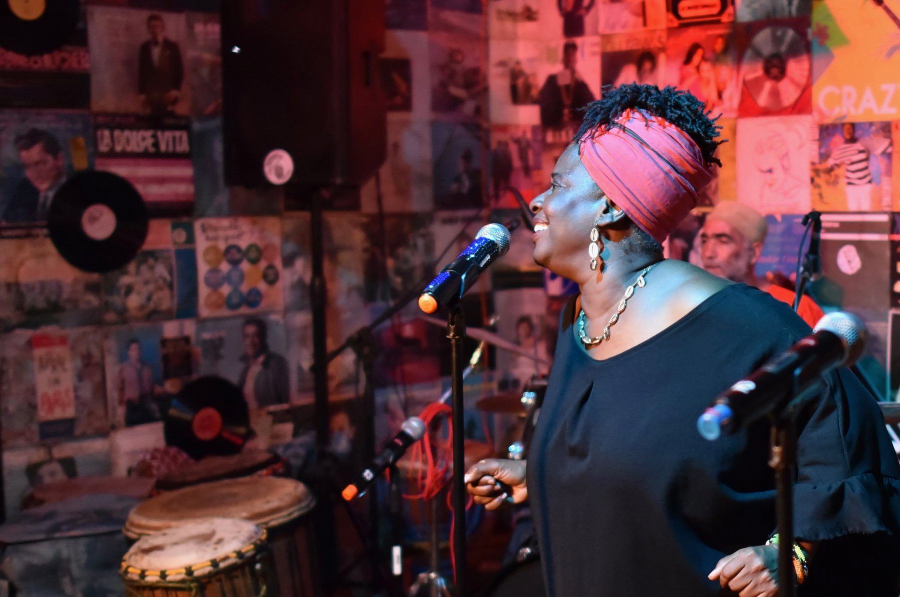 A woman is singing into a microphone in front of a wall of records.