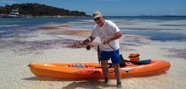 A man is fishing from a kayak on the beach