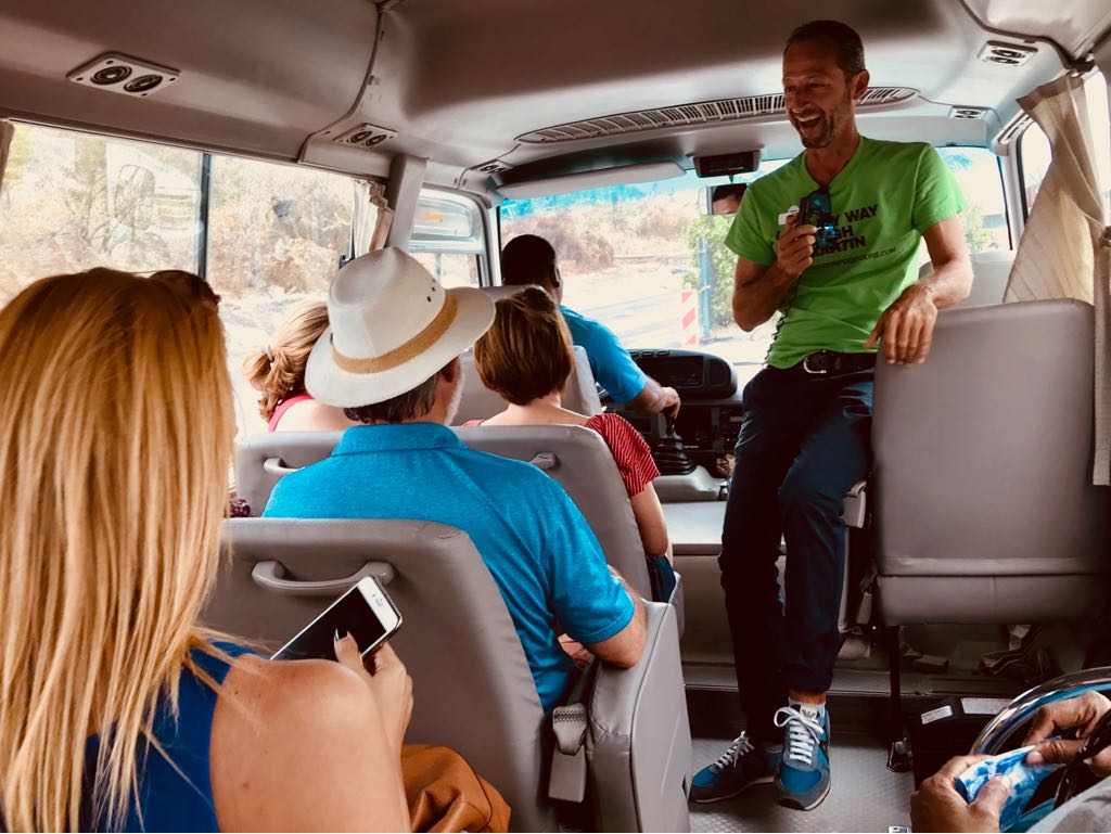 A man in a green shirt is talking to a group of people on a bus.