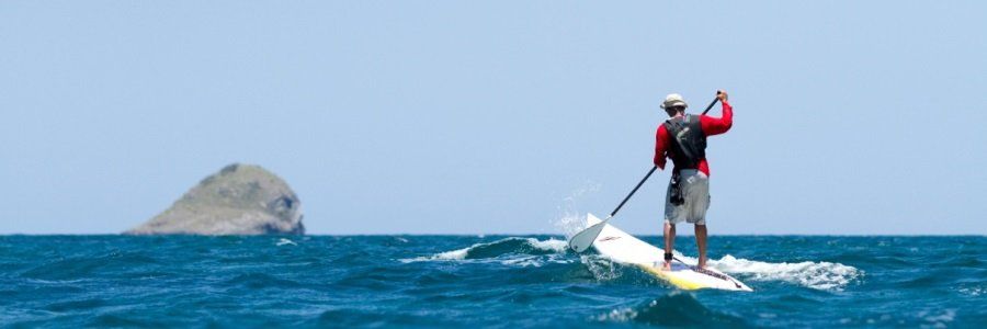 A man is standing on a paddle board in the ocean.