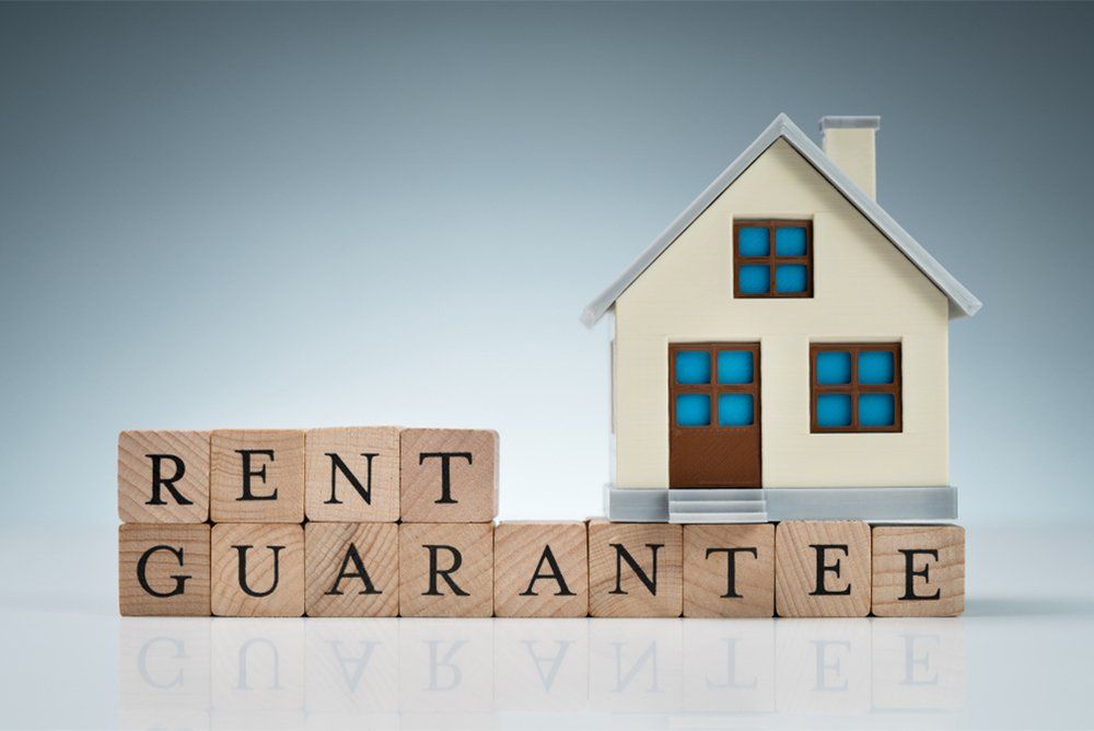 Close-up Of Small House Model On Wooden Blocks With Rent Guarantee Text Over Table