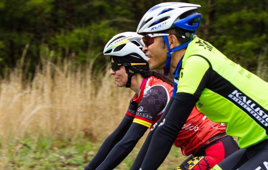 Two cyclists wearing helmets and sunglasses are riding down a road.