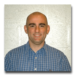 A bald man wearing a blue plaid shirt is smiling for the camera.