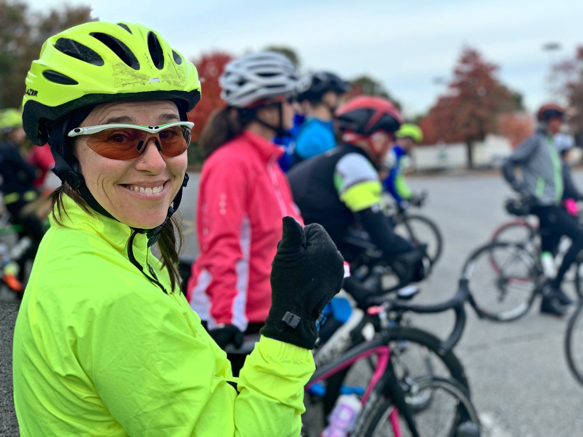 A woman wearing a yellow helmet and sunglasses is giving a thumbs up.