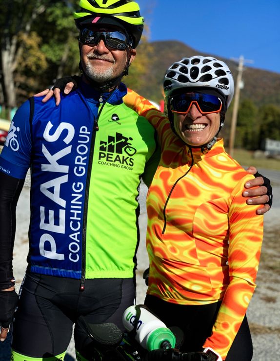 A man and a woman are posing for a picture and the man is wearing a peaks coaching group shirt