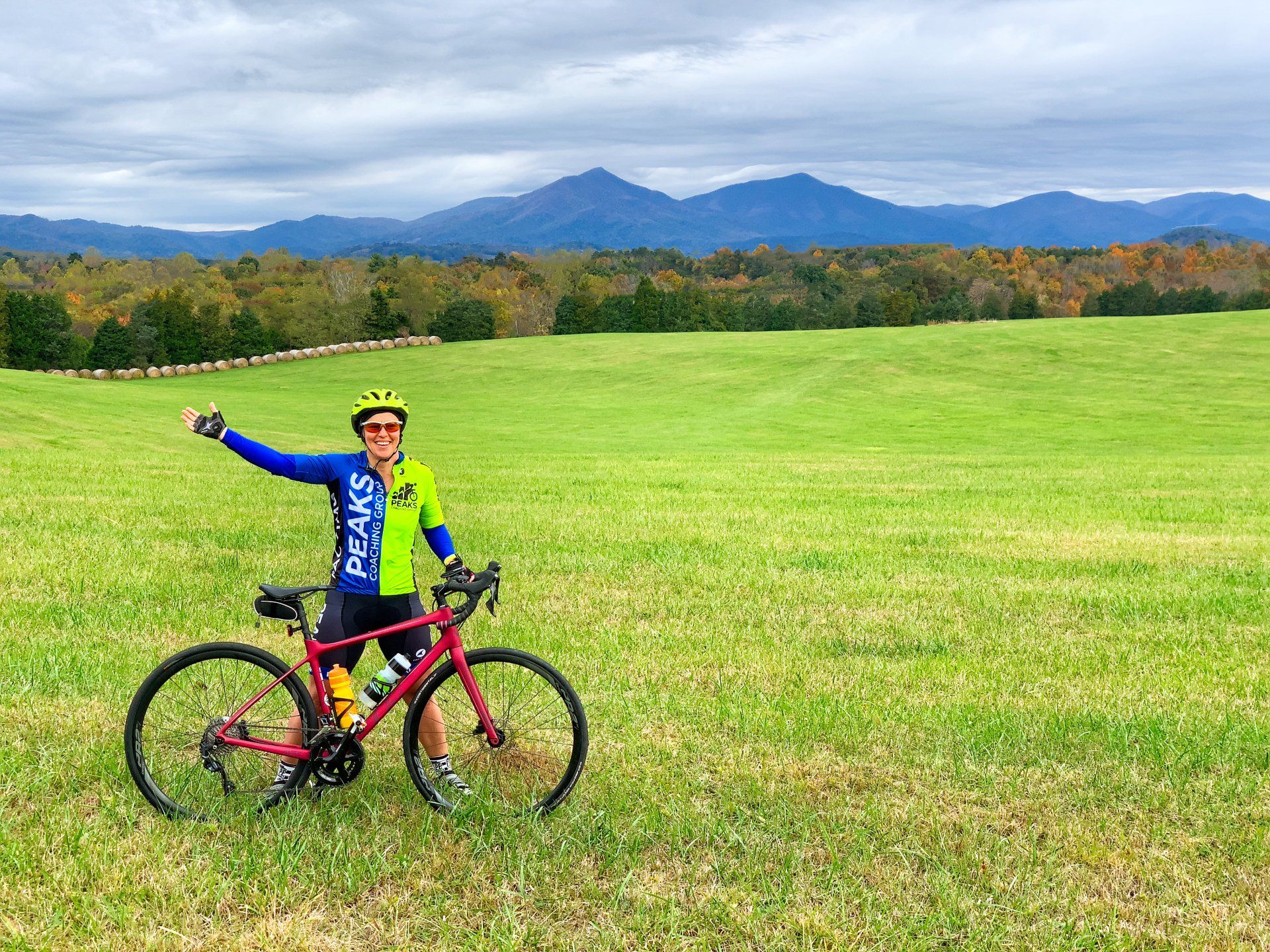 A person is standing next to a bicycle in a field with mountains in the background.