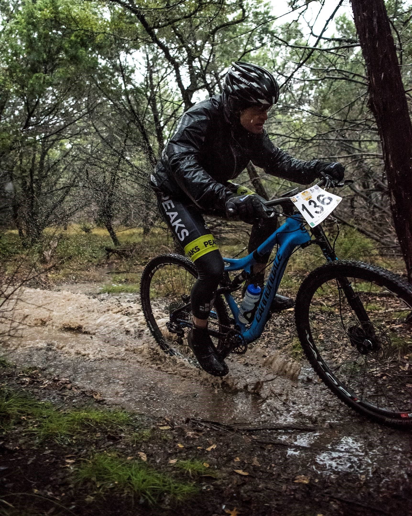 A man is riding a mountain bike down a muddy trail in the woods.
