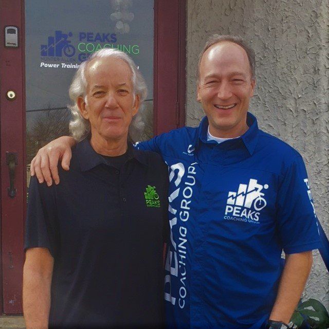 Two men are posing for a picture in front of peaks coaching