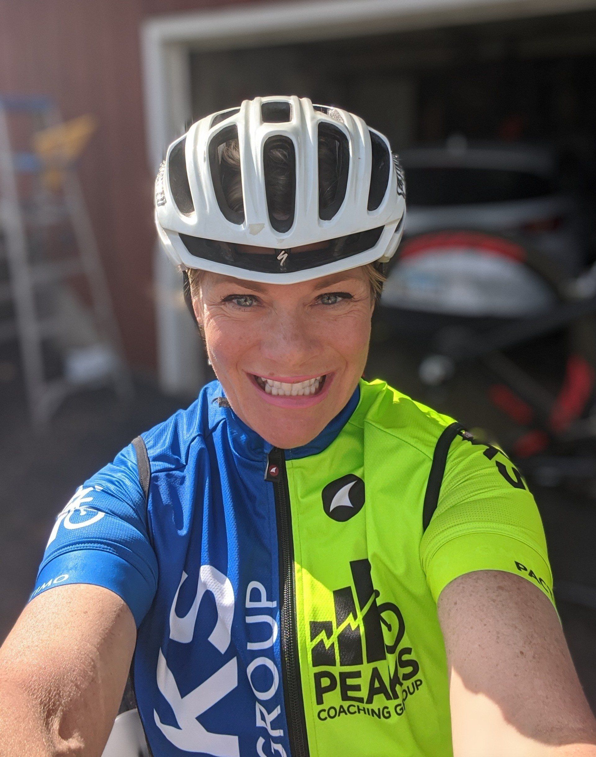 A woman wearing a helmet and a cycling jersey is smiling.
