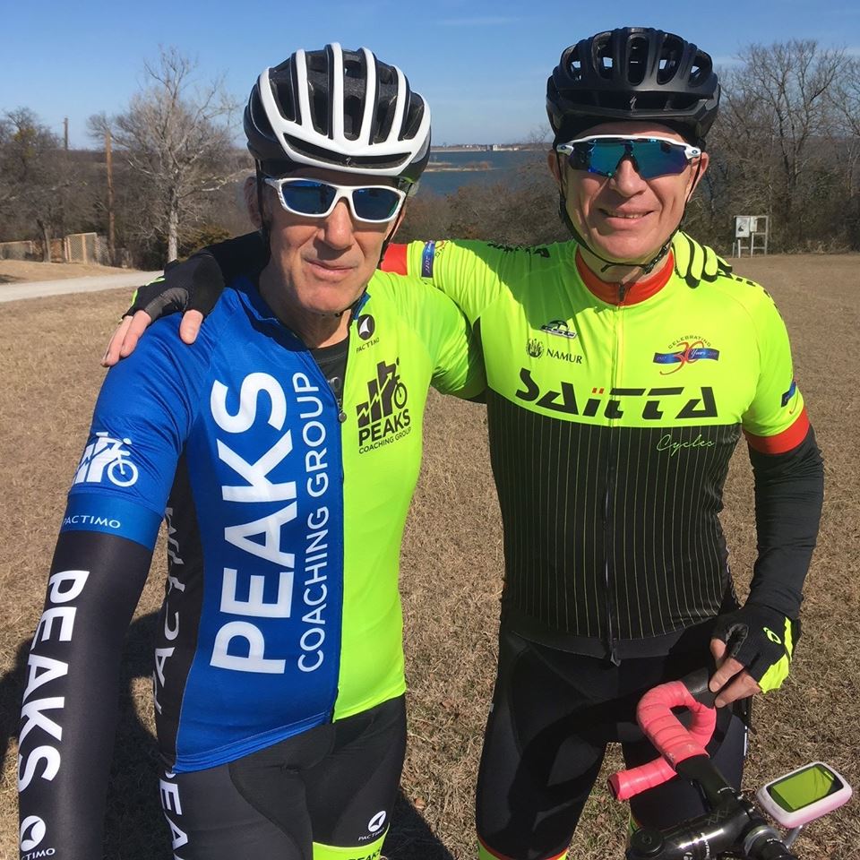 A man wearing a peaks coaching group jersey stands next to another man