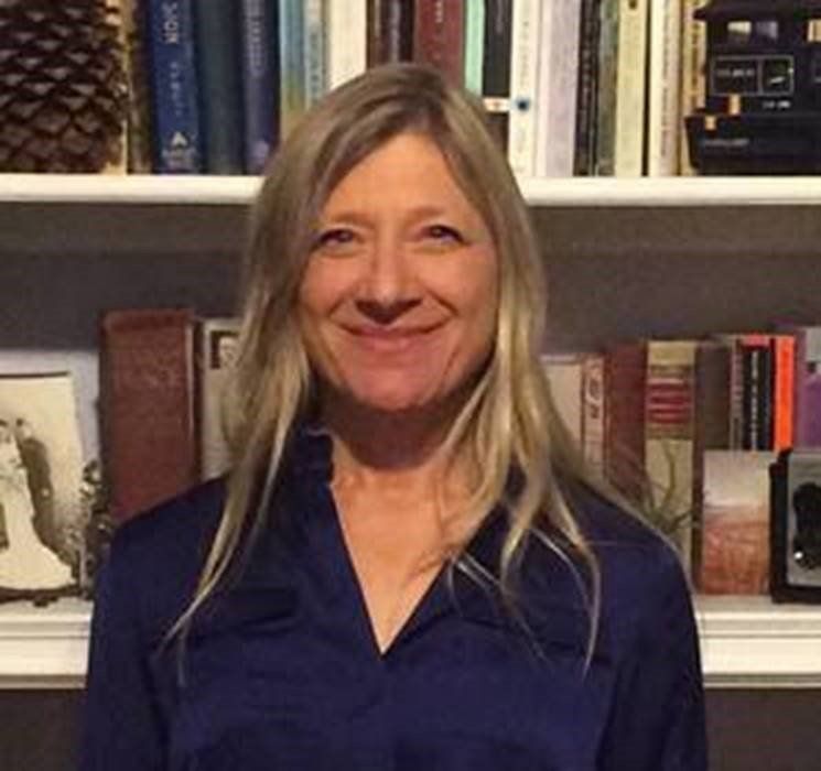 A woman is smiling in front of a bookshelf filled with books.